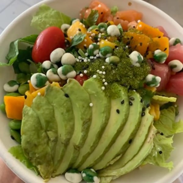 A colorful poke bowl with avocado slices, cherry tomatoes, mango, and green peas.