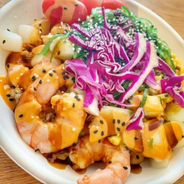 Close-up of a colorful poke bowl with shrimp, red cabbage, seaweed, and sauce.