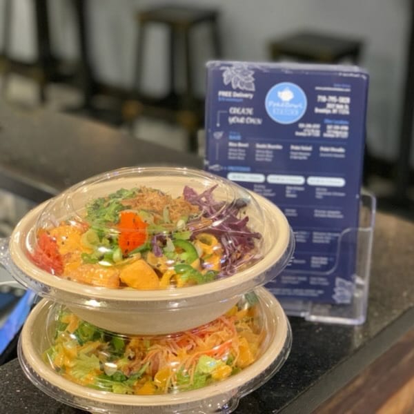 Two stacked poke bowls with colorful ingredients and a menu stand in the background.