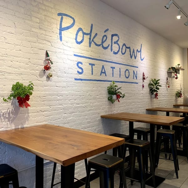 Interior of Pokebowl Station with white brick walls, wooden tables, black stools, and festive decorations.