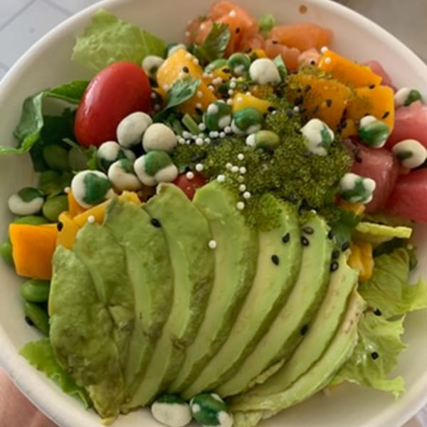 A vibrant poke bowl with sliced avocado, tuna, mango, tomatoes, and green seaweed pearls.