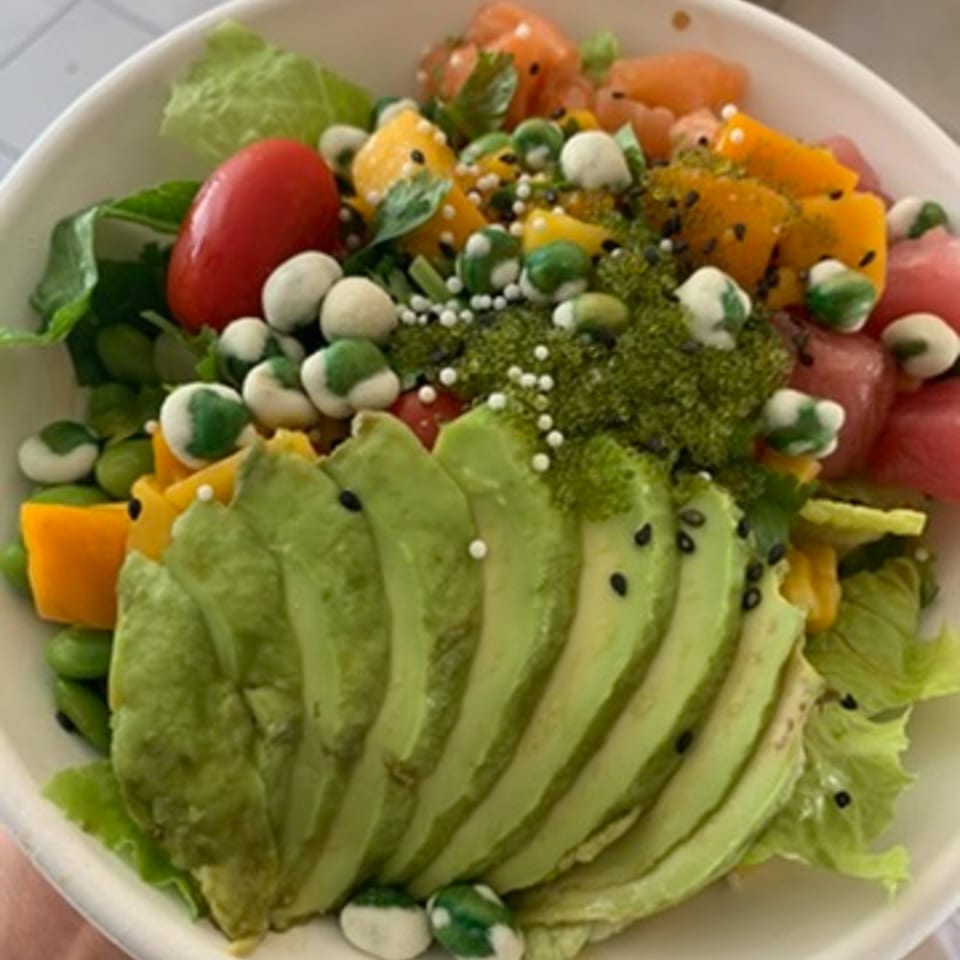 A vibrant poke bowl with sliced avocado, tuna, mango, tomatoes, and green seaweed pearls.