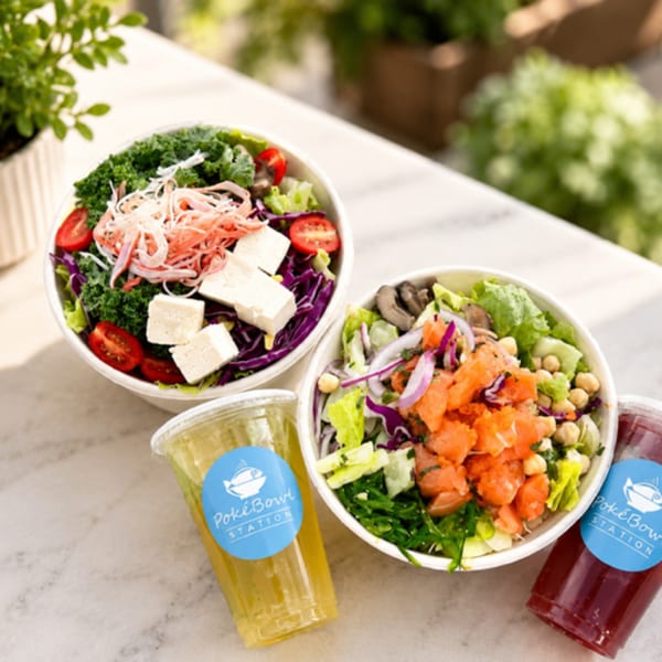 Two colorful poke bowls with drinks from Poke Bowl Station on a white table outdoors.