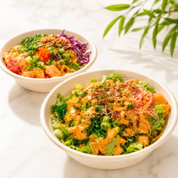 Two colorful poke bowls with various toppings, including salmon, greens, and sauces, on a marble surface.