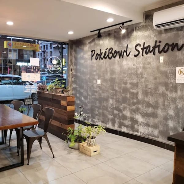 Interior of PokiBowl Station with a wooden table, chairs, plants, and a textured gray wall.