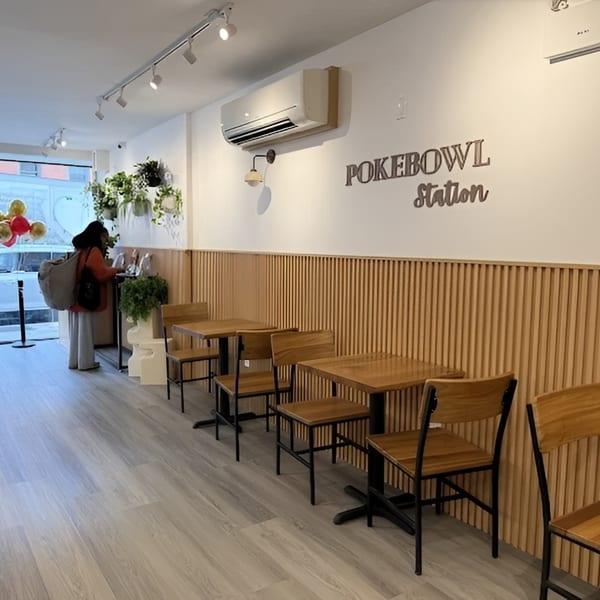 Interior of Pokebowl Station with wooden tables and chairs, light wood paneling, and a customer at the counter.