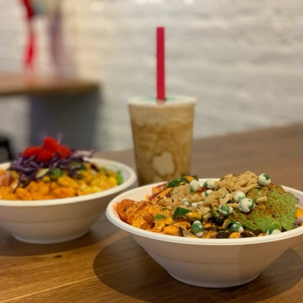Two colorful poke bowls and a drink with a red straw on a wooden table.
