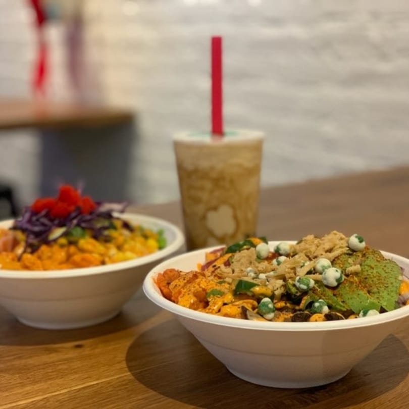 Two colorful poke bowls and a drink with a red straw on a wooden table.