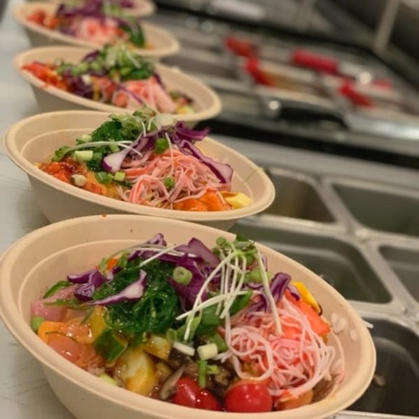 Multiple colorful poke bowls with various toppings like seaweed, crab, and vegetables, lined up on a counter.