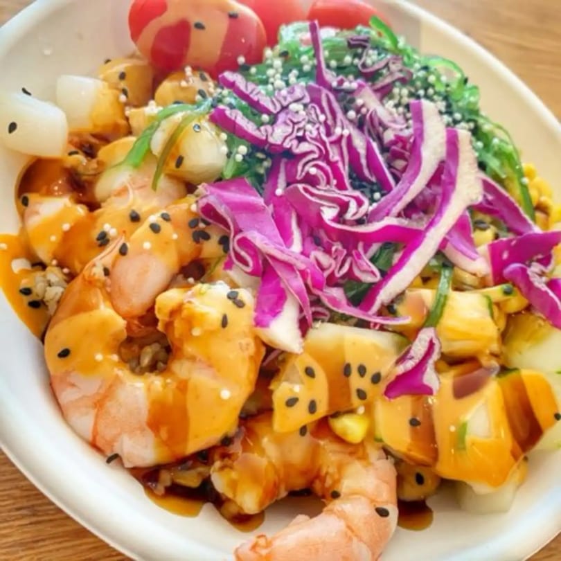 Close-up of a colorful poke bowl with shrimp, red cabbage, seaweed, and sesame seeds.