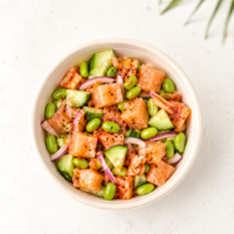 Overhead view of a poke bowl with salmon, edamame, cucumber, and red onion.